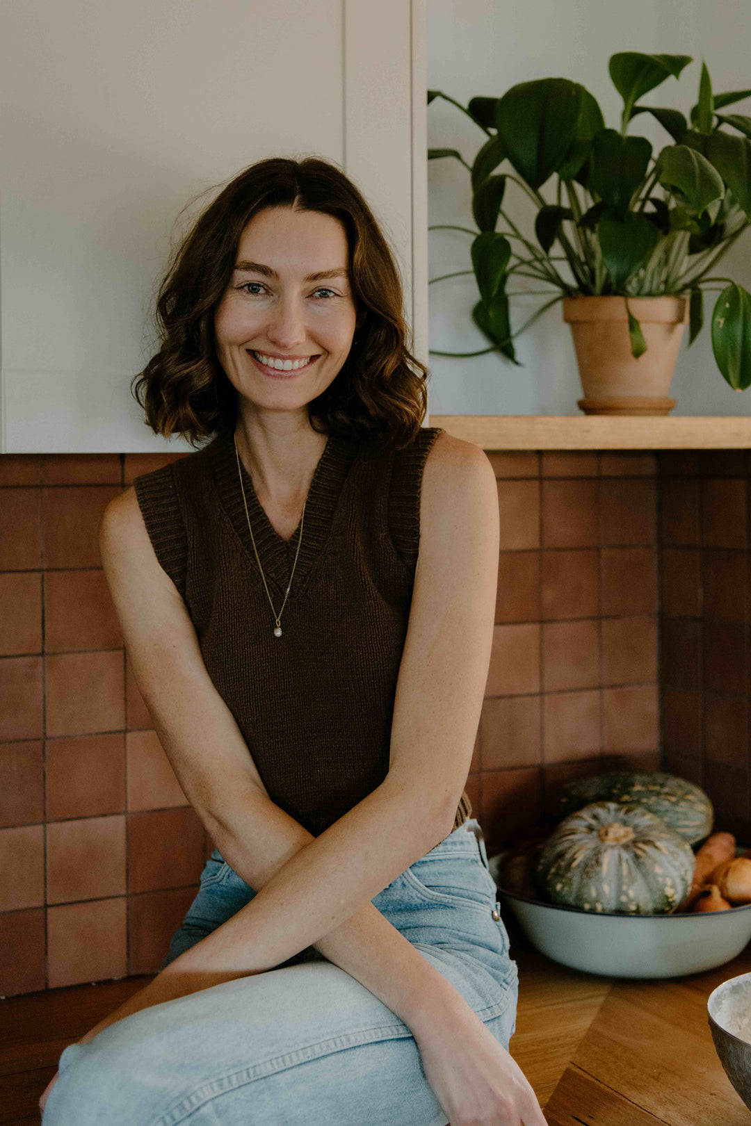 Woman sitting in a cozy room with a plant and pumpkins in the background